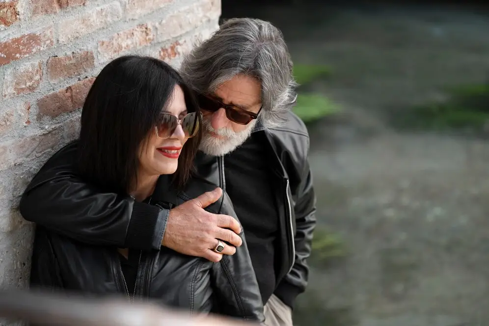 Foto hombre abrazando a una mujer que está sonriendo, están arrecostados a en una pared. Representando el artículo de Lovitmatch making.